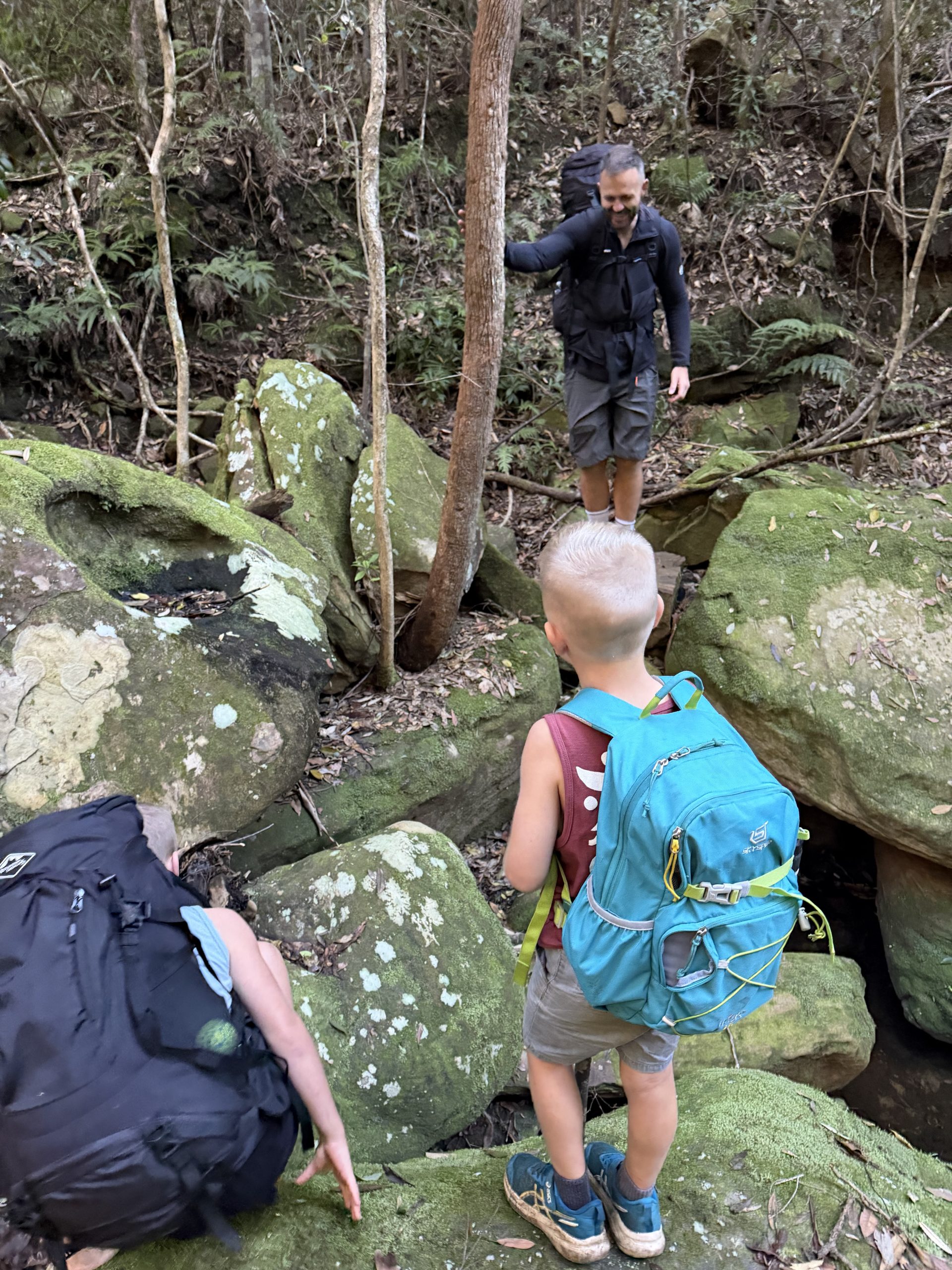 The kids climbing over boulders with their packs on