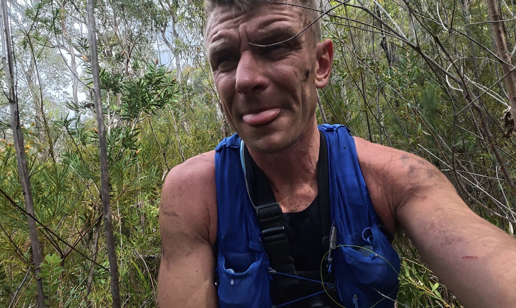 Close up selfie of Nathan, scratched and dirty, pulling a face in thick bush