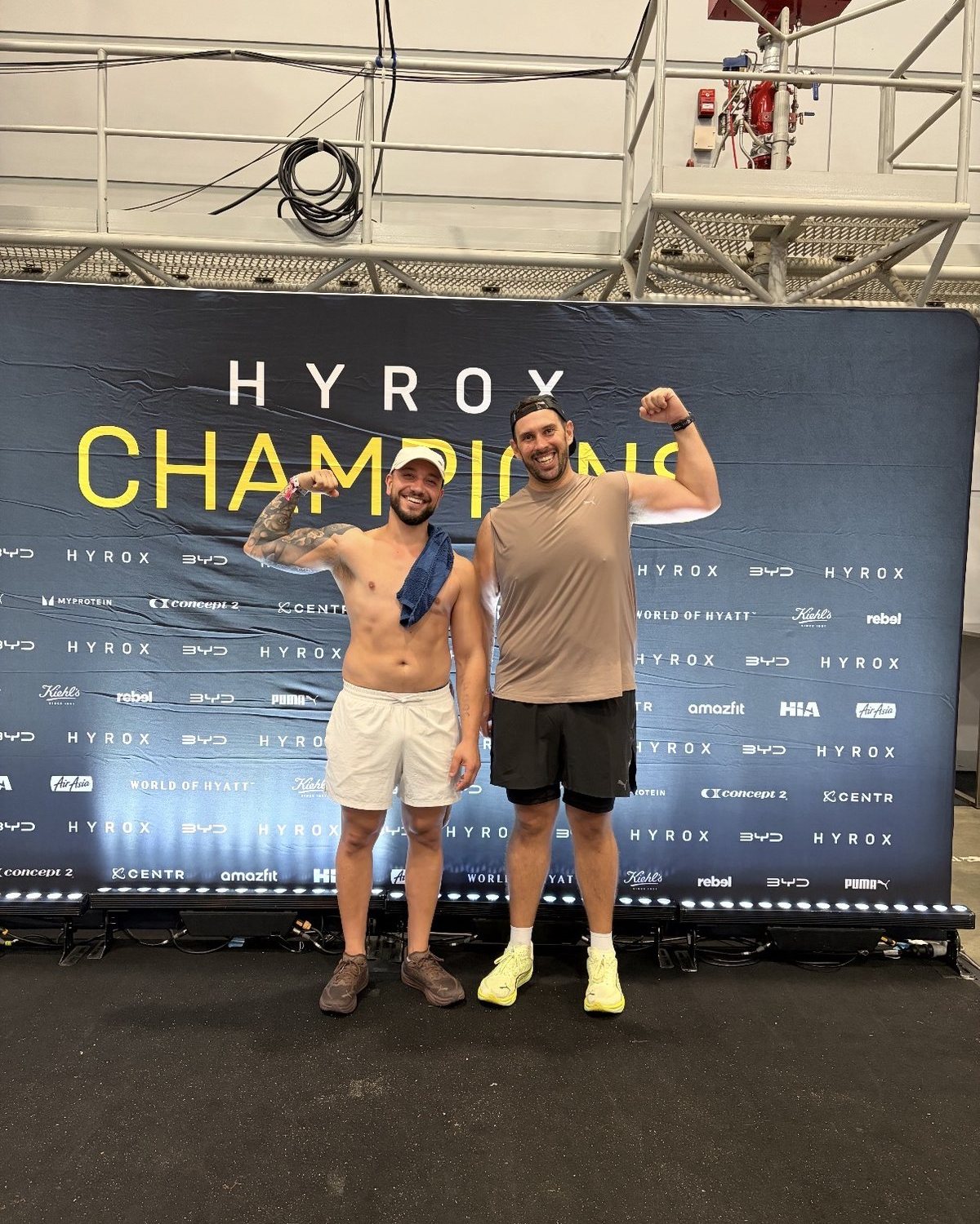 Berdo flexing in front of the HYROX Champions backdrop with a training partner after his race
