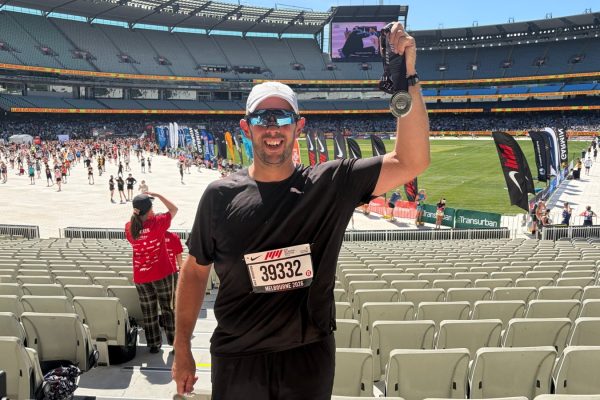 Berdo holding up his Melbourne Half Marathon medal at the MCG
