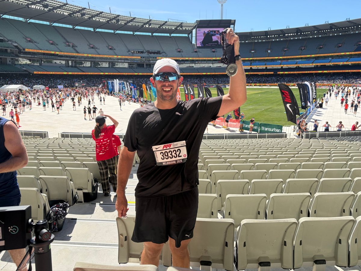 Berdo holding up his Melbourne Half Marathon medal in the stands at the MCG
